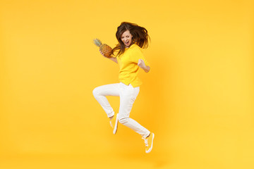 Fototapeta na wymiar Screaming young woman in casual clothes doing winner gesture jumping hold fresh pineapple fruit isolated on yellow orange background. People vivid lifestyle relax vacation concept. Mock up copy space.