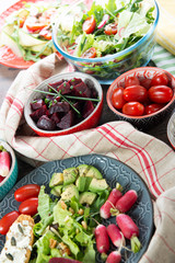 bowls and plate of healthy vegan salad . Various vegetables avocado,  cucumber, radishes on wooden background
