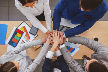 Top view of business people stacking hands above desk. On desk paperwork, laptops and smart phones.Knowledge is being aware of what you can do. Wisdom is knowing when not to do it.