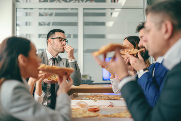 Business people sitting at boardroom and having pizza for lunch.