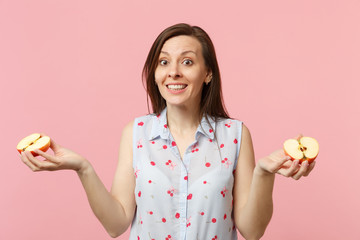 Smiling young woman in summer clothes holding in hands halfs of fresh ripe apple fruit isolated on pink pastel background in studio. People vivid lifestyle, relax vacation concept. Mock up copy space.