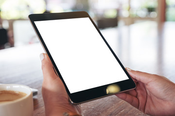 Mockup image of hands holding black tablet pc with blank white screen with coffee cup on wooden table