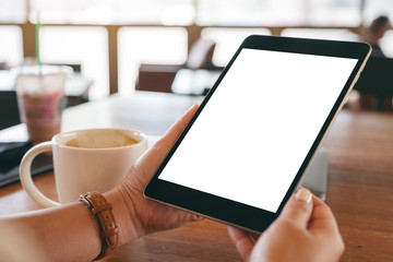 Mockup image of hands holding black tablet pc with blank white screen with coffee cup on wooden table