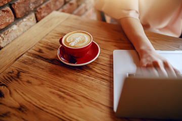 Close up of Caucasian woman typing on keyboard while sitting in restaurant. On desk coffee.