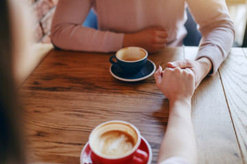 Young couple in love sitting in cafeteria and holding hands. On desk cups with coffee.