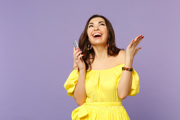 Cheerful young woman in summer dress using mobile phone, typing sms message, spreading hands, looking up isolated on violet background. People sincere emotions, lifestyle concept. Mock up copy space.