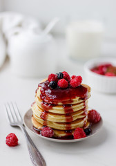 Plate with delicious pancakes with raspberries and berry sauce on white background.