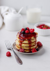 Plate with delicious pancakes with raspberries and berry sauce on white background.