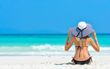 Sexy woman in bikini enjoy tropical vacation. Girl in hat relaxing on summer holiday. Girl with perfect sexy sport body in bikini Resting relaxing on the white sand tropical beach near sea.