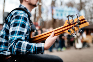 Photo of musician playng on six string fretless bass guitar on the street in front of people.
