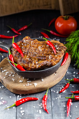 grilled kebab grilled meat steak lies in an iron frying pan, on a wooden vintage old board rustic,...