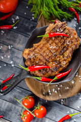grilled kebab grilled meat steak lies in an iron frying pan, on a wooden vintage old board rustic,...