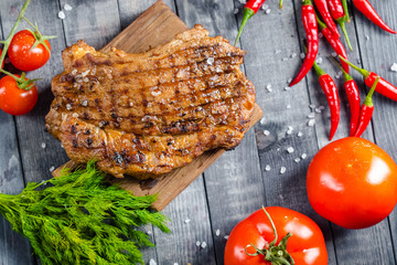 grilled kebab grilled meat steak lies on a wooden vintage old board rustic, chili, with tomatoes,...