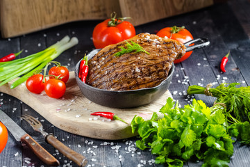 grilled kebab grilled meat steak lies in an iron frying pan, on a wooden vintage old board rustic,...