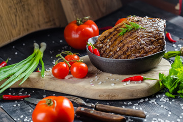 grilled kebab grilled meat steak lies in an iron frying pan, on a wooden vintage old board rustic,...