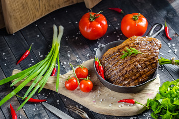 grilled kebab grilled meat steak lies in an iron frying pan, on a wooden vintage old board rustic,...