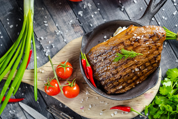 grilled kebab grilled meat steak lies in an iron frying pan, on a wooden vintage old board rustic,...