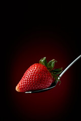 Strawberry in spoon on a dark background.