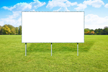 Blank advertising billboard in a green field with trees and sky on background - image with copy space