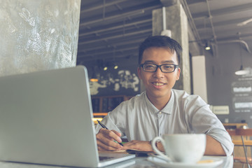 Smiling Asian freelancer writing notes at cafe