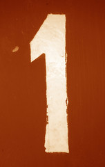 Number 1 in stencil on metal wall in orange tone.