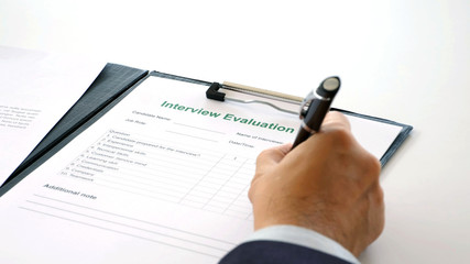 Man hand checking the interview evaluation paper for job interview at office background, job search, business concept