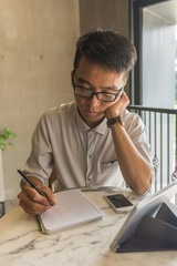 Fototapeta na wymiar Asian freelancer thinking and writing into notes