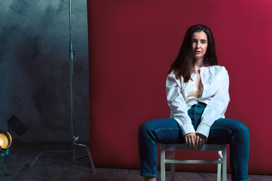 model tests of a young girl. A beautiful girl is dressed in blue jeans and a white shirt, with a button splayed and visible bus balter. On the background a tripod and a bardovy background with a retro