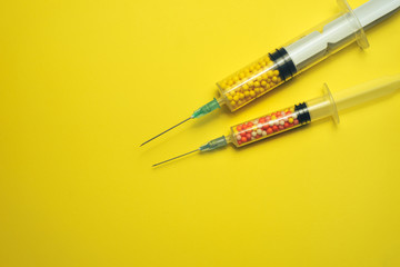 Two syringe filled with colorful nano balls on a yellow background. Innovative medical concept. ...