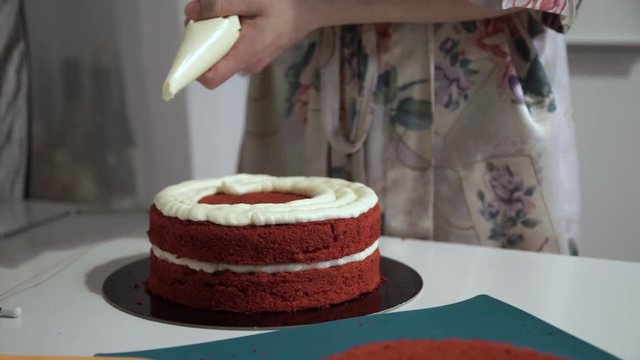 Making red velvet cake at home. Smearing layer of cake cream.