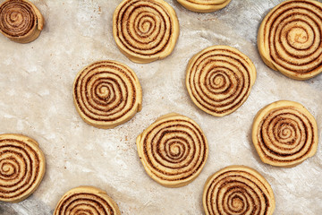 Blanks of cinnamon rolls dough are on greased parchment paper