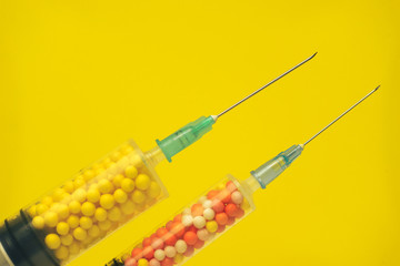 Two syringe filled with colorful nano balls on a yellow background. Innovative medical concept. ...