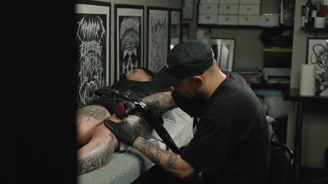 Master tattoo draws the orange paint on the clients tattoo. Tattoo artist holding tattoo machine in black sterile gloves