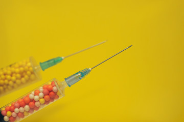 Two syringe filled with colorful nano balls on a yellow background. Innovative medical concept. ...