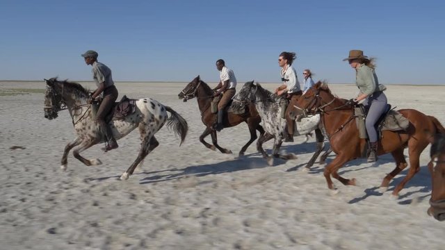 Slow motion view of a group of horse riders having fun galloping across the wide open spaces of the Makgadikgadi salt Pans 