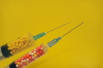 Two syringe filled with colorful nano balls on a yellow background. Innovative medical concept. ...