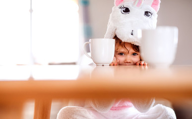 A portrait of small girl in unicorn mask sitting at the table at home.