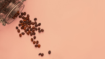 Arabica coffee beans spill out of a glass jar on a pink monophonic background, close-up, day