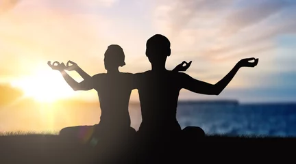 Poster mindfulness, spirituality and outdoor yoga - silhouettes of couple meditating in lotus pose over sunset and sea background © Syda Productions