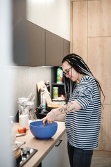 smiling dreadlock girl  in striped blouse cooking on the kitchen