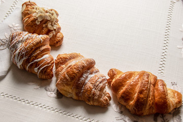 freshly baked croissants with almonds, chocolate and powdered sugar on a table with napkins and tablecloth, closeup, top view caps