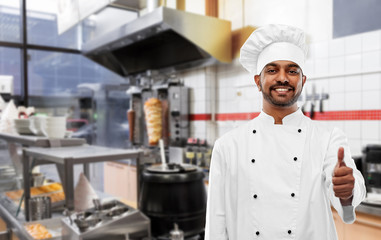 cooking, profession and people concept - happy male indian chef in toque showing thumbs up over kebab shop kitchen background