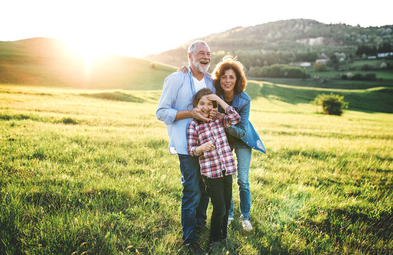 Senior Couple With Granddaughter Standing Outside In Spring Nature At Sunset.