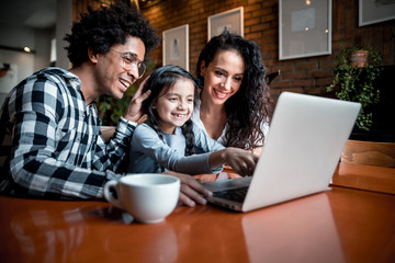Happy multiethnic family having fun while using laptop together at restaurant