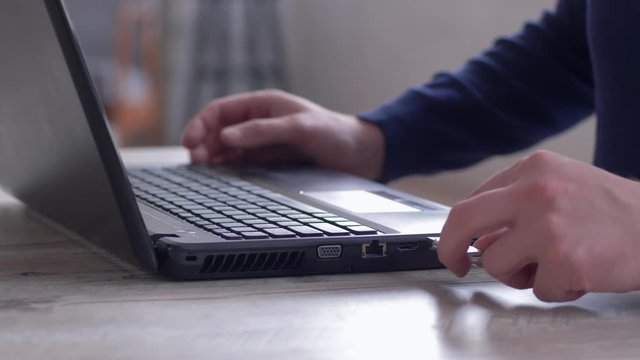 male hands uses laptop and copying information to usb flash drive sitting at the table