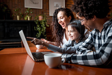Happy multiethnic family having fun while using laptop together at restaurant