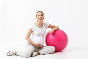 Beautiful young pregnant yoga fitness woman posing isolated over white wall background make exercises with ball.