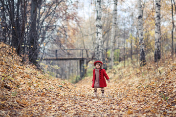 Fototapeta premium Child girl in red coat and hat walks autumn forest