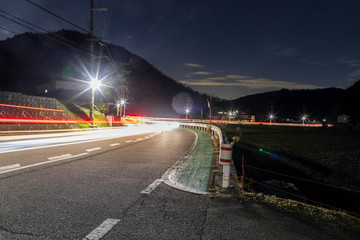 Car lights blur by curve on quiet country road at night