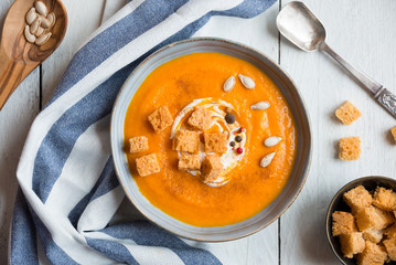 Delicious pumpkin soup in a bowl with croutons on white wood